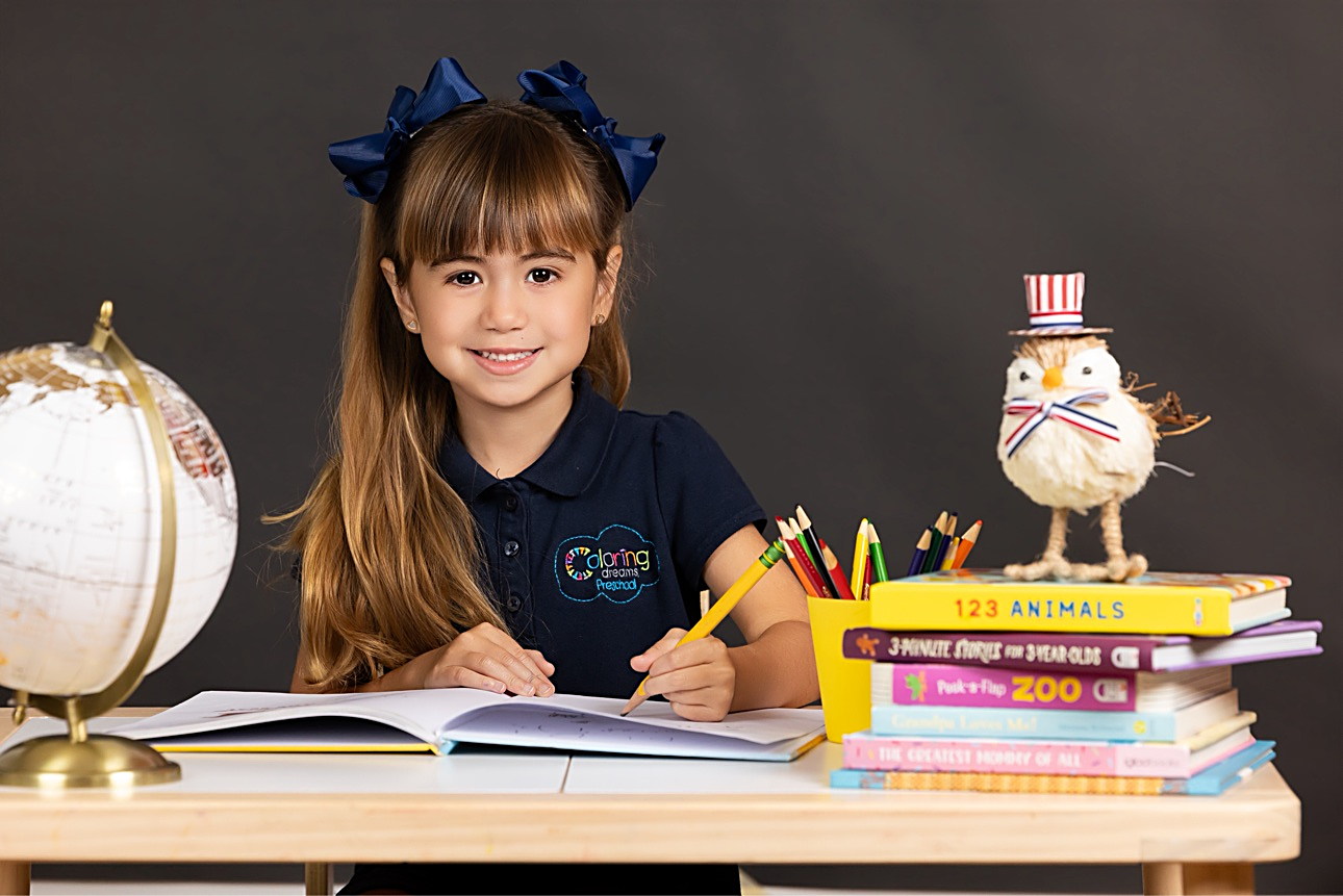 Niña en su escritorio el Día de la Foto, con globo terráqueo y libros