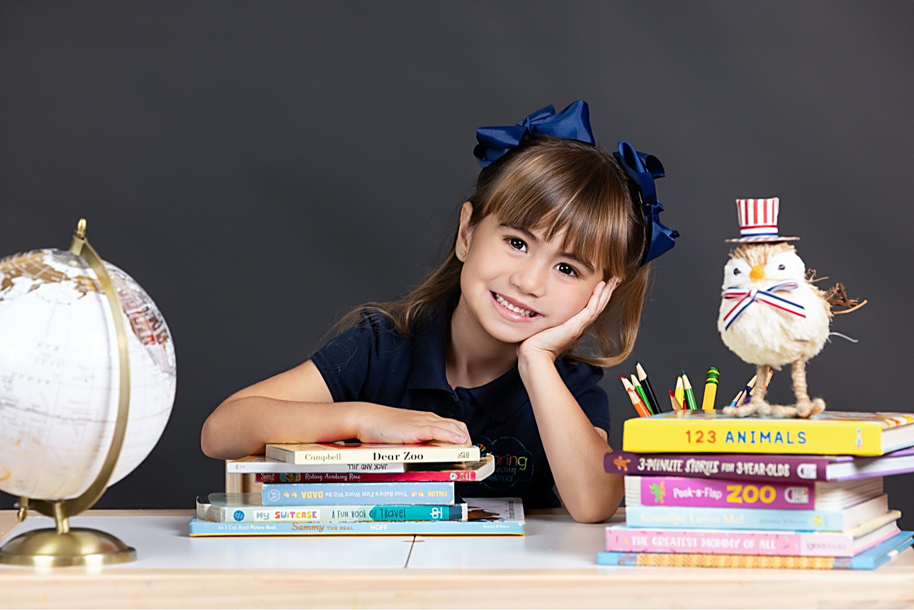 Niña sonriendo apoyada en una pila de libros en el set de Picture Day